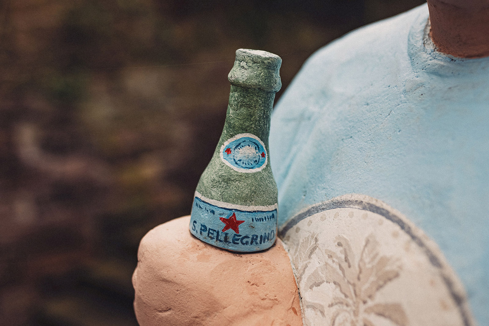 Die Hand einer Alltagsmenschen-Figur in Großaufnahme, sie hält eine San Pellegrino-Flasche
